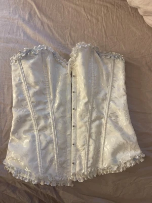 Vit korsett - Vitt korsett, perfekt till halloween. mönstrad och band i ryggen som man kan knyta med har dock en liten fakeblod fläck som säkert går bort i tvätten. 