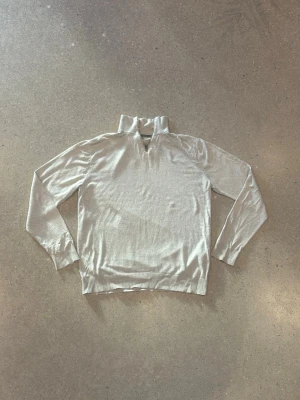 Beige half zip tröja från Jack & Jones - Snygg beige långärmad tröja från Jack & Jones i storlek M. Tröjan har en hög krage med half zip-dragkedja och är tillverkad i mjuk stickad bomull. Perfekt för lager-på-lager och chill stil. Ribbstickade muddar vid ärmslut och nederkant.