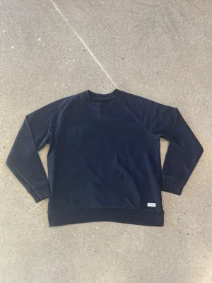 Mörkblå sweatshirt från 157 Denim Makers - Snygg mörkblå sweatshirt från 157 Denim Makers i storlek M. Tröjan har klassisk rund hals, ribbade muddar vid ärmslut och nederkant samt en diskret etikett framtill. Perfekt för chill dagar och enkel att matcha med jeans eller joggers.