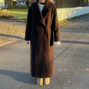 Mörkbrun lång kappa med knappar slutsåld junkyard - Stilren mörkbrun kappa med klassisk krage och enkel knäppning framtill. Det är ull i materialet vilket gör den varm till vintern!Lång modell med rak passform och diskret slits bak. Perfekt för dig som gillar en clean och tidlös look. Helt slutsåld på junkyard. Brukar ha S men denna i XS passar mycket bra. Använd ca 10 gånger därav i super skick
