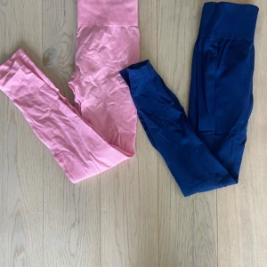 STRNGTH leggings rosa & marinblå - Två par leggings från STRNGTH, ett i ljusrosa och ett i marinblått. Båda har bred, ribbad hög midja med logga framtill. Stretchigt och mjukt material som sitter tight och följer kroppen, perfekt för gymmet eller chill. Snygg och enkel design utan mönster. Båda tightsen har scrunch som framhäver baksidan mycket bra!🩷💙storlek XS/S