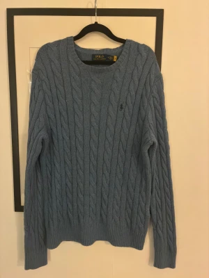 Blå stickad tröja från Polo Ralph Lauren - Polo Ralph Lauren kabelstickad tröja i storlek M. Blå, klassisk modell med broderad logga. Bra skick, inga defekter. Varm och skön Perfekt nu till vintern