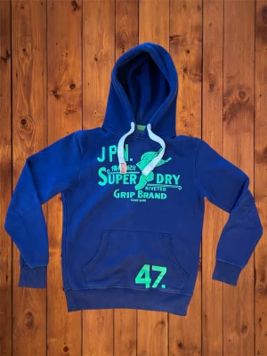 Vintage Superdry Hoodie - Säljer denna vintage asfeta hoodien från Superdry. Den är riktigt fet och har en snygg design med feta detaljer. Storlek är S och passar som S/M se måtten nedan. B=67cm A=54cm