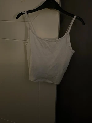 Vit ribbad linnetopp - Säljer en enkel och fräsch vit linnetopp med smala axelband. Toppen är ribbad och har en croppad passform som passar perfekt till jeans eller kjol. Materialet känns mjukt och lätt, perfekt för varma dagar.