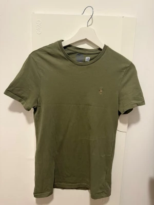 Olivgrön t-shirt från Polo Ralph Lauren - Säljer en olivgrön t-shirt från Polo Ralph Lauren med klassisk rund hals och liten broderad logga på bröstet. Modellen är Custom Slim Fit. Som helt ny!