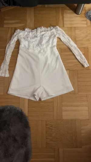 Vit spetsig byxdress från SHEIN - Säljer en vit byxdress från SHEIN i storlek M. Den har långa ärmar i spets och axelbandslös design upptill, medan byxdelen är slät och kort. Perfekt för dig som gillar en chic och trendig look med snygga detaljer.