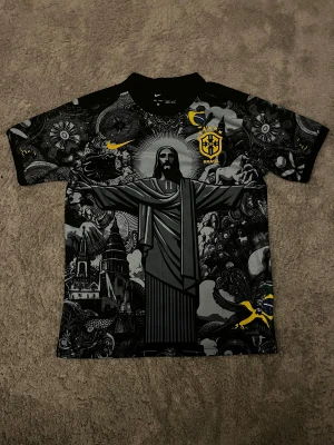Nike Brasil fotbollströja svart/gul - Snygg Brasilien fotbollströja från Nike med svart och grått grafiskt mönster, stora trycket av Kristusstatyn och detaljer i gult. Broderad CBF-logga och Nike Swoosh på bröstet. Materialet är lätt och andas, perfekt för fotboll eller streetwear.