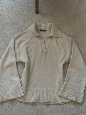 Beige stickad tröja från Gina Tricot - Säljer en beige stickad tröja från Gina Tricot med breda ribbade muddar och krage med v-ringad öppning. Tröjan har lång ärm och är perfekt för lager-på-lager under hösten och vintern. Mjuk och skön kvalitet som känns lyxig.