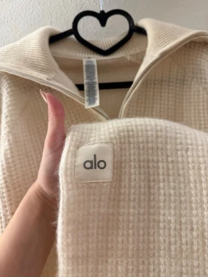 Beige stickad tröja från Alo+ byxor - Säljer en beige stickad tröja från Alo med grov struktur och bred krage. Plus byxorna till. Sytt ett litet hål i fram och de är lite kortare i längden. 