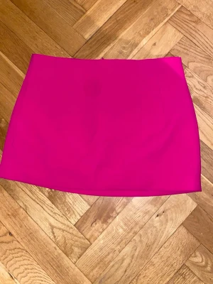  Zara kjol - Säljer en snygg knallrosa kortkjol från Zara i storlek XL. Kjolen har en rak och stilren form med dragkedja bak. Materialet är slätt och känns som polyester, vilket ger en cool och modern vibe. Perfekt för dig som gillar färgstarka plagg och vill sticka ut.