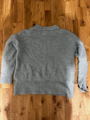 Grön stickad tröja med ribbad kant - Mysig grön stickad tröja med lång ärm och ribbad kant vid nederdelen och ärmsluten. Tröjan har en enkel design med rund hals och passar perfekt för kyliga dagar. Skön och klassisk stil som är lätt att matcha med jeans eller andra favoritplagg.