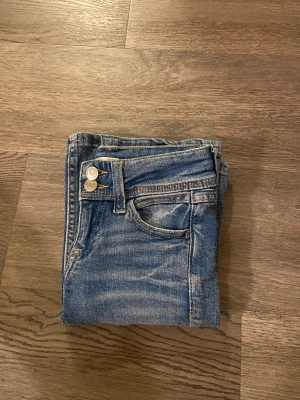 Blåa jättefina jenas - Snygga blå jeans från Gina Tricot med klassisk femficksdesign. Jeansen har två silverfärgade knappar i midjan och coola slitningar för en trendig look. Materialet är slitstarkt denim och bakfickorna har broderad detalj.