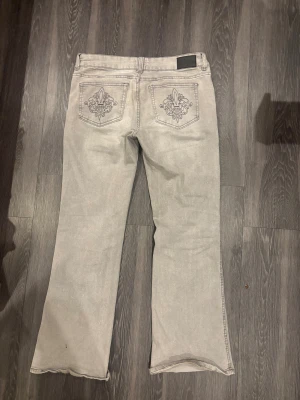 Grå bootcut jeans från lager 157 - Snygga grå jeans från lager 157 med bootcut passform och broderade detaljer på bakfickorna. Jeansen har låg midja och är tillverkade i mjukt bomullsmaterial. Perfekt för dig som gillar stilrena jeans med lite extra detaljer.