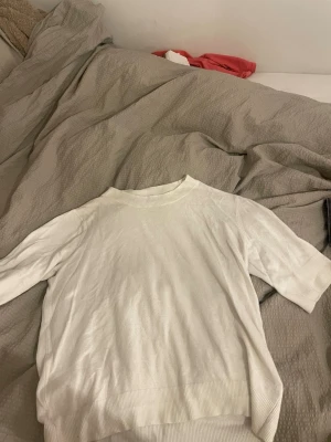 Vit stickad tröja från 157 - Säljer en vit stickad tröja från 157 i storlek S. Tröjan har ribbade muddar vid hals, ärmslut och nederkant samt korta ärmar. Enkel och clean design som funkar till många olika stilar. Perfekt för dig som gillar minimalistiskt.