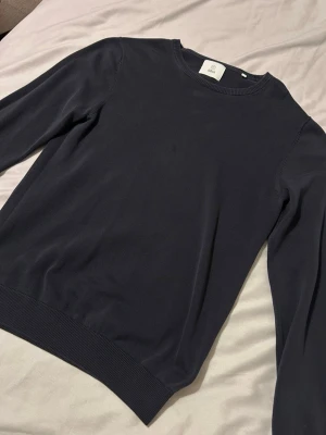 Mörkblå tröja från Bläck - Snygg mörkblå tröja från bläck i klassisk modell med rund hals och långa ärmar. Tröjan är tillverkad i mjuk bomull och har ribbade muddar vid ärmslut och nederkant. Perfekt för dig som gillar stilrena och enkla plagg.