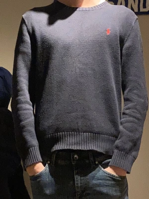 Mörkblå stickad tröja Polo Ralph Lauren - Säljer en mörkblå stickad tröja från Polo Ralph Lauren i storlek M. Tröjan har rund hals, ribbade muddar och en röd broderad logga på bröstet. Bra skick passar dig runt 180cm. Skriv vid frågor!