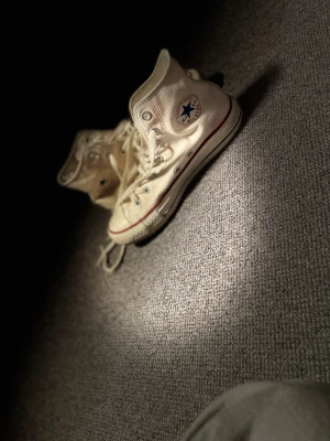 Vita Converse Chuck Taylor All Star - Säljer ett par klassiska vita Converse Chuck Taylor All Star high-tops med röd rand och blå logga på sidan. Skorna har snörning, rund tå och är tillverkade i canvas med gummisula. Perfekta för en avslappnad och cool stil. Har lite rosa fläckar på sidan men det är inget man ser så jätte tydligt. Det är bara att skriva till mig om det är någonting du undrar över! 