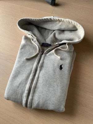 Grå ziphoodie från Ralph Lauren - Säljer en mycket fin hoodie från Ralph Lauren. Jag är 177cm och väger 62kg. Storlek S. Mycket bra skick, inga defekter som hål eller fläckar.
