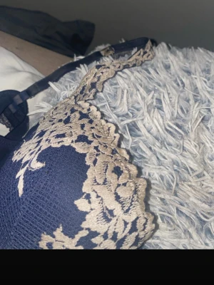 Mörkblå spetsbroderad bh - Snygg mörkblå bh med vit spetsbroderi i blommigt mönster över kuporna och axelbanden. Bh:n har justerbara axelband och klassisk hakknäppning bak. Materialet är mjukt och stretchigt med en elegant finish. Den är väldigt smutsig men jag är ganska säker på att det går att tvätta bort men vill man ha den skickat fort så kommer jag ej att tvätta den så kommer man behöva tvätta den själv. Vill man att jag ska tvätta den kommer det ta lite längre tid.köpt i somras så har haft i några månader.