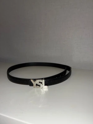 Svart skinnbälte - Snyggt svart skinnbälte med en snygg silver logga och en väldigt snygg design runt hela beltet.