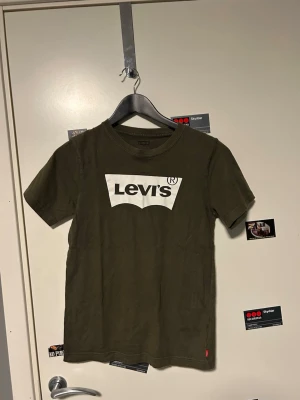 Olivgrön Levi's t-shirt med logga - Säljer en olivgrön t-shirt från Levi's med klassisk vit logga framtill. T-shirten har rund halsringning och korta ärmar. Tillverkad i mjuk bomull som känns skön mot huden. Perfekt för dig som gillar enkel och stilren streetwear.
