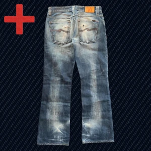 Nudie Jeans Bootcut Ola Rich Blue - Ett par riktigt snygga Nudie Jeans Bootcut Ola! Storlek på taggen: 34/32 (Se mått nedan). Fint skick, har slitningar och patina från användning, t.ex två mindre hål i båda bakfickor. Skriv om du har frågor!  Mått: Storlek på tag – 34/32, Midja – 43 cm, Lår – 28 cm, Innersöm – 80 cm, Längd – 105 cm, Benöppning – 23.5 cm