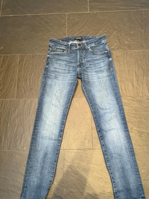 Blå skinny jeans från Jack & Jones - Snygga blå skinny jeans från Jack & Jones med klassisk femficksdesign och slitna detaljer. orginal pris är 1200! Jeansen har normal midja och är tillverkade i stretchigt denim för skön passform. Perfekta för dig som gillar en chill outfit. jeanses passar med en skön snygg hoodie