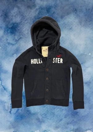 Vintage Hollister Cardigan Med Knappar - Väldigt sällsynt och vintage Hollister hoodie med knappar | Tröjan är i väldigt bra skick utan defekter! | Längd ≈ 63cm, Bredd armhåla-amrhåla ≈ 53cm | Modell 175cm, 68kg | Hör av vid ytterligare frågor och priset kan diskuteras vid snabbt köp! |