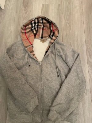 Grå Burberry Zip Hoodie - Burberry zip up hoodie i grå, använd sparsamt. Skriv om du funderar något!