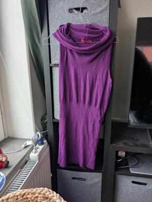 Lila ärmlös klänning med krage - Säljer en lila klänning med snygg hög krage och ärmlös design. Klänningen är figurnära och har en mjuk, stickad känsla i materialet. Perfekt för dig som gillar färgstarka plagg med enkel siluett och cool detalj vid halsen.
