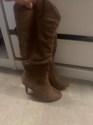 Bruna stövlar med klack från Anna Field - Säljer ett par snygga bruna stövlar från Anna Field i storlek 40. De har en hög klack och är gjorda i mjuk mocka med rund tå. Perfekt för dig som vill ha en stilren look med lite extra höjd. Dragkedja på sidan för enkel påtagning.