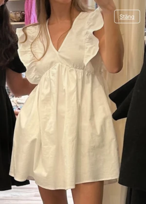 Klänning med volang - Supersöt vit klänning med v-ringning, volangdetaljer vid axlarna och kort längd. Finns även fickor! Lånade bilder och säljer pga den inte passade mig