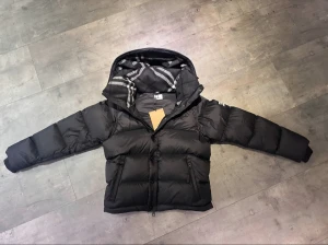 Burberry Puffer  - Svart dunjacka från Burberry med klassisk Säljer en elegant och mångsidig Burberry-jacka i svart, i nyskick. Dunfodrad för värme och komfort med det klassiska rutmönstret i huvan som ger en exklusiv touch. Praktiska dragkedjefickor, avtagbar huva och diskret logopatch på ärmen. Passar M/S. Jackan är i princip som ny och utan defekter. En lyxig kombination av stil och funktion – perfekt för både vardag och tillfällen då du vill klä upp dig.  📦Snabb leverans - skickas samma dag📌.