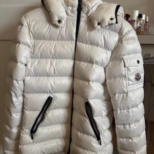 Vit dunjacka från Moncler med luva!!💕 - Säljer en snygg vit dunjacka från Moncler med huva och svarta dragkedjor. Jackan är köpt 2022 på moncler hemsida. Köpt för ca 7000 kr. Jackan är i barn storlek (164) men passar även mig som bär storlek xs/s. 