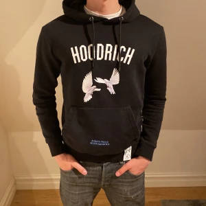 Svart hoodie från Hoodrich - Säljer en svart hoodie från Hoodrich med tryck av vita fåglar och text både fram och bak. Hoodien har en känguruficka och justerbar huva med snören. Perfekt för en avslappnad stil. Tröjan var limited edition och säljs inte längre. Modellen är 183 och det står att tröjan är XS men väger mer åt S/M pris är diskuterbart👍