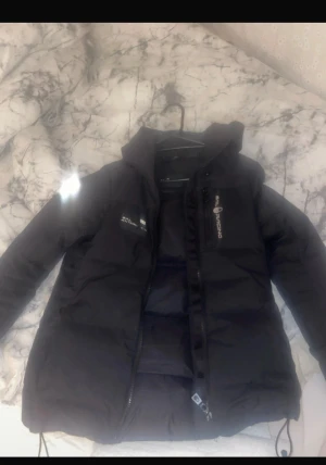 Svart pufferjacka från Sail Racing XS - Svart pufferjacka från Sail Racing i storlek XS. Jackan har luva , dragkedja framtill och logga på bröstet och ärmen. Snygg, stilren och perfekt för kalla dagar. Det går ha till tjejer eller killar möts i Eskilstuna 
