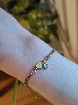 Armband med berlock - Guldigt armband med berlock. Stainless steel. Armbandet är helt nytt. Fick tyvärr hem armbandet med fel initialer så jag har ingen användning av detta, säljer det och hoppas någon annan kan glädjas av detta fina armband.