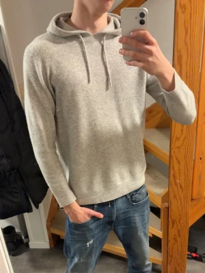 Kashmir hoodie - Säljer en stilren ljusgrå Kashmir hoodie med huva och snörning. Tröjan har långärmade ärmar och en mjuk, stickad känsla. Perfekt för chill dagar och enkel att matcha med jeans eller joggers. Snygg och enkel design som funkar året runt. 