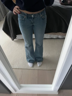 Bootcut ljusblå jeans - Säljer ett par klassiska ljusblå jeans med bootcut passform. Jeansen har låg midja, fem fickor och råa, fransiga benslut för en avslappnad vibe. Tillverkade i mjukt denimtyg som sitter snyggt över höften och låret och släpper ut vid vaden.