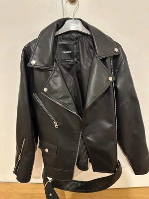 Svart skinnjacka från Pull&Bear - Snygg svart skinnjacka från Pull&Bear med klassisk bikerstil. Jackan är onanvänd