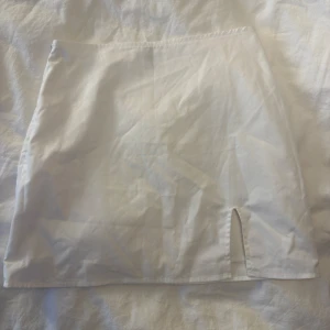 Vit kortkjol med slits - Enkel och stilren vit kortkjol med liten slits framtill. Kjolen har rak passform och är perfekt för dig som gillar minimalistisk stil. Tillverkad i ett lätt tyg som känns skönt mot huden.