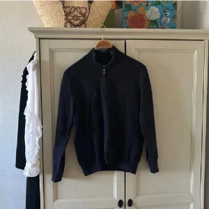Marinblå half zip tröja Polo Ralph Lauren - Snygg marinblå stickad tröja från Polo Ralph Lauren med half zip och hög krage. Tröjan har långärmad passform och är tillverkad i mjuk bomull. Perfekt för dig som gillar klassisk stil med en modern touch.