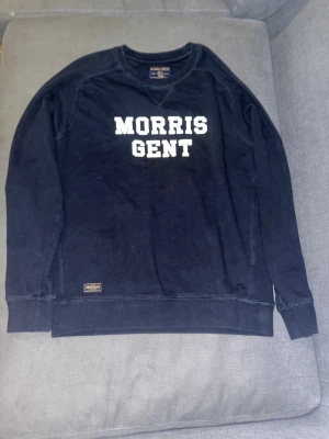 Mörkblå sweatshirt från Morris Gents - Snygg mörkblå sweatshirt från Morris Gents med vit text på bröstet. Tröjan har rund hals, långa ärmar och ribbade muddar vid ärmslut och nederkant. Klassisk och stilren design med diskret Morris-märke nedtill.