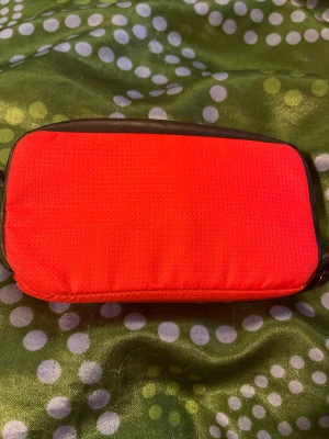 Röd plånbok från Everest - Snygg röd plånbok från Everest med svart kant och dragkedja. Tillverkad i slitstark polyester och har ett praktiskt fack på insidan. Perfekt storlek för att ha med sig i väskan eller fickan. Enkel och stilren design med Everest-logga på framsidan.passar som mobil väsk 