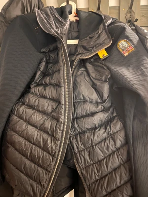 Svart pufferjacka Parajumpers XL - Säljer en svart pufferjacka från Parajumpers, modell Warm Up. Jackan har quiltad framsida och rygg, huva, dragkedja och coolt PJS-märke på ärmen. Materialet är polyester och syntet, perfekt för kalla dagar. Snygg och sportig look med detaljer i orange. endast använd 2 månader och sedan legat i garderobet, priset är inte fast skriv gärna privat för mer info!