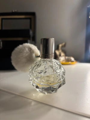 Ariana Grande parfym med puff - Snygg parfymflaska från Ariana Grande med en fluffig vit puff som detalj. Perfekt för dig som vill ha en trendig och unik accessoar på sminkbordet. Volym och ingredienser syns ej på bilderna.