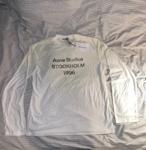 Vit långärmad Acne Studios tröja - Vit långärmad tröja från Acne Studios med tryck 'Acne Studios STOCKHOLM 1996' i svart på bröstet. Rund hals och mjukt bomullsmaterial. Perfekt för dig som gillar clean och stilren design med en touch av street. Storlek M men sitter som L. lnte 0rglnal 😊