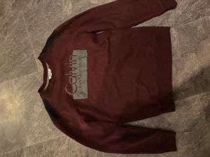 Vinröd sweatshirt från Calvin Klein Jeans - Snygg vinröd sweatshirt från Calvin Klein Jeans med svart detalj på axlarna och stort tryck på bröstet. Otroligt bra skick i storlek small. Pris kan diskuteras!😊