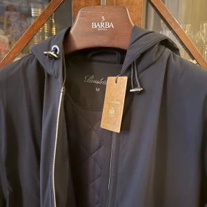 Stenströms jacka - Svart vindjacka från Stenströms med huva och snygg quiltad insida. Jackan har dragkedja framtill, snörning vid huvan och två praktiska fickor. Perfekt för dig som gillar stilren och funktionell design. Svårt med färgen antingen väldigt mörkblå eller svart. 5000kr från butik. Helt ny. 