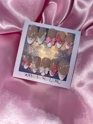 SweetFrench (XS);Medium Almond - Säljer ett set press-on naglar i almondform med handmålade franska tippar, dekorerade med 3D rosetter, pärlor och blommor i vitt och rosa. Naglarna har en nude bas och detaljer som hjärtan och pärlsträngar för en extra söt look. Perfekt för dig som vill ha unika och kreativa naglar.XS: 14 mm, 11 mm, 11,5 mm, 10 mm, 8 mm  
